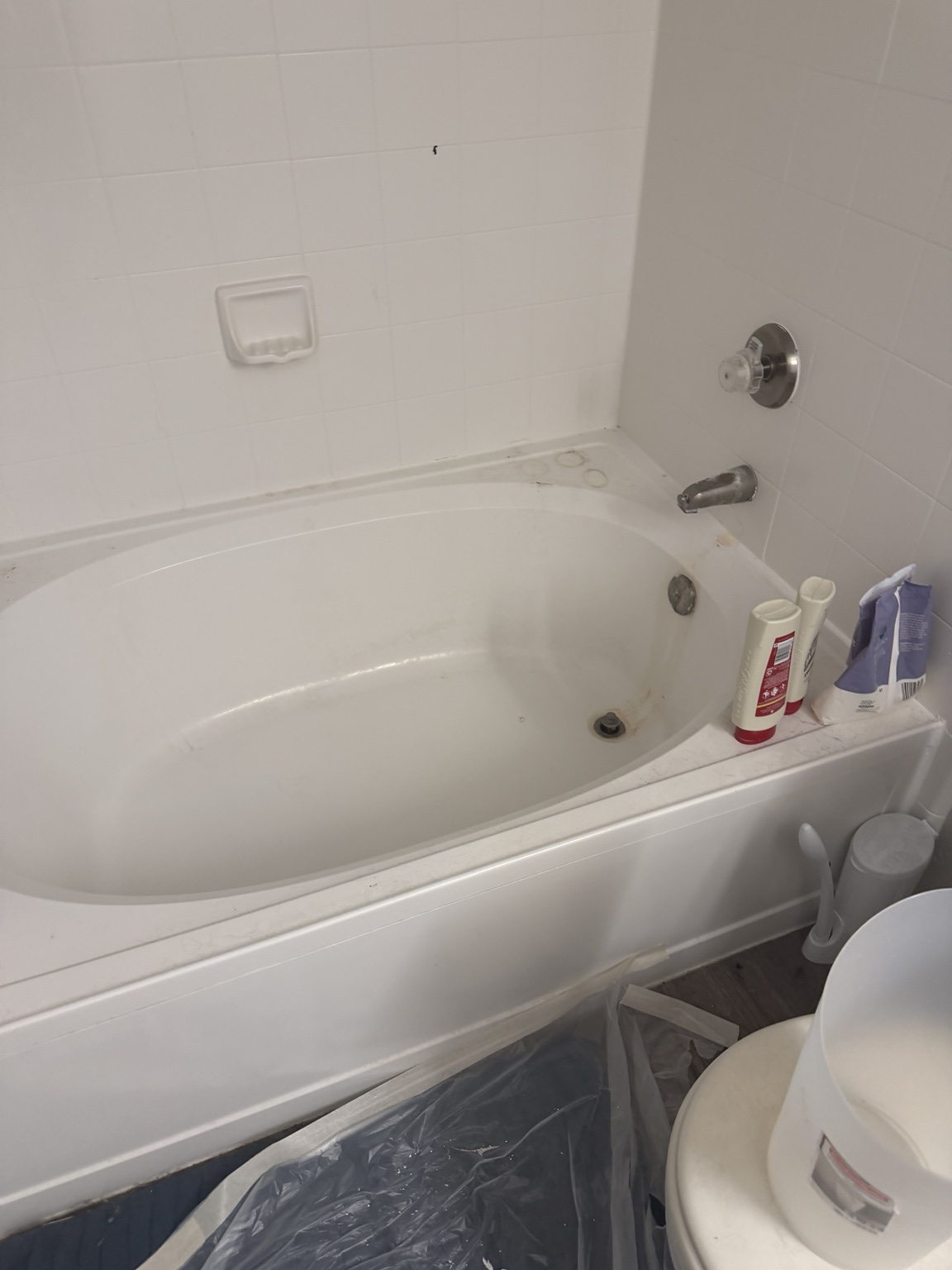 Before: bathtub with visible marks and bottles along the ledge